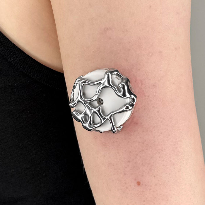 A close-up of a person's forearm wearing a chunky silver ring with a white circular center and organic, raised silver patterns.