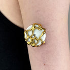 A close-up of a person's forearm wearing a large circular ring with a white center and an abstract gold filigree-like border.